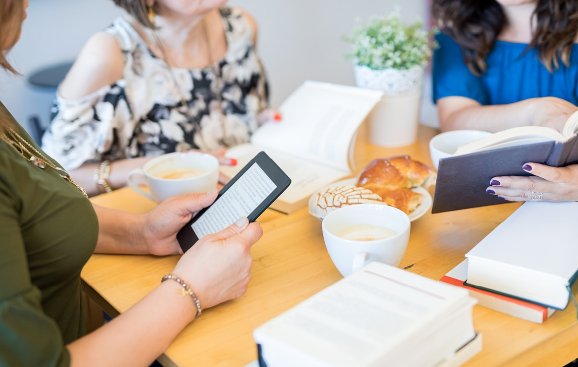 hands holding ebook and physical books at table