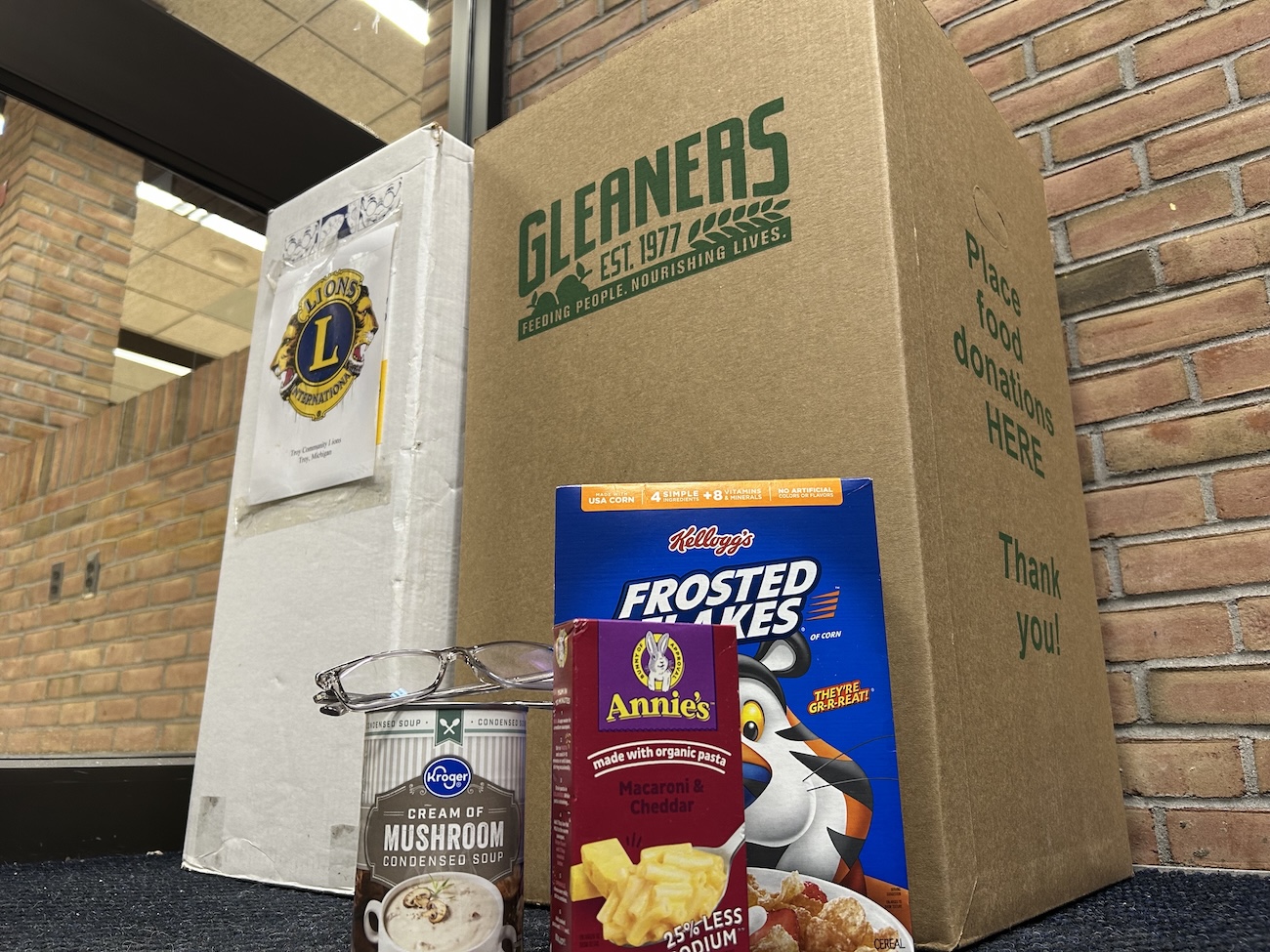 Donation items of food and glasses in front of donation boxes for Gleaners and Lions Club